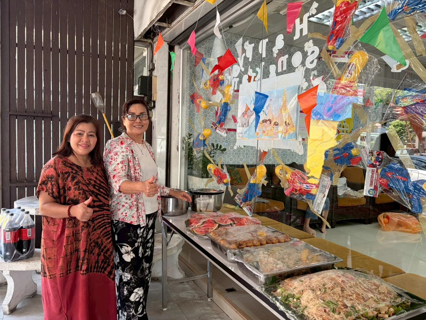 Two women posing by the table of food during Songkran